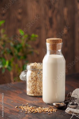 Vegan oat milk  non dairy alternative milk in a glass. Oat flakes  on wooden table.
