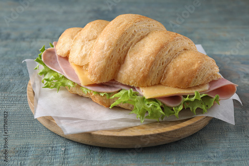 Tasty croissant sandwich with ham on light blue wooden table