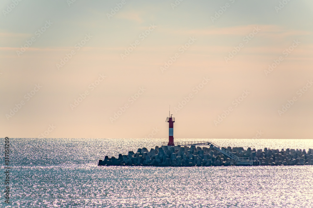 Clear sky and bright orange sunset over the sea with a breakwater and a lighthouse