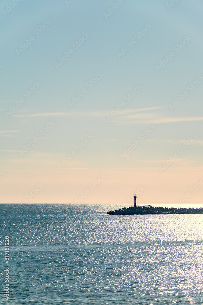 Clear sky and bright sunset over the sea with a breakwater and a lighthouse