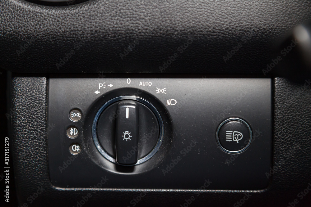 Close-up on the headlight switch control buttons and automatic adjust level dashboard in car in the back of a suv after cleaning and detailing in the vehicle repair workshop. Auto service industry