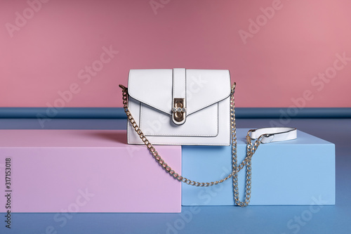 A small women's rectangular handbag on a chain strap stands on a pink, blue stand. Studio photo photo