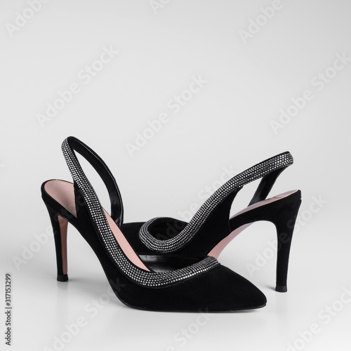 Womens black suede heeled shoes with shiny rhinestone trim on top and a heel strap. Close-up side view. On a white background for a catalog