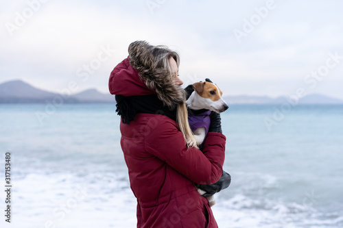 Love for pets. Jack Russell Terrier dog sitting in the arms of the mistress on the background of the sea landscape. Weekend with a dog