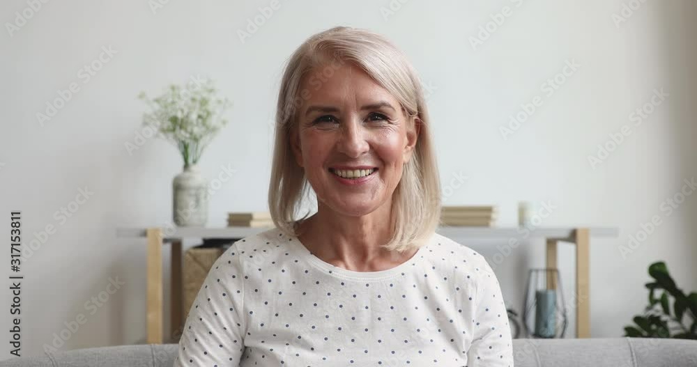 Happy middle aged woman talking to camera sit on sofa Happy middle aged woman talking to camera sit on sofa