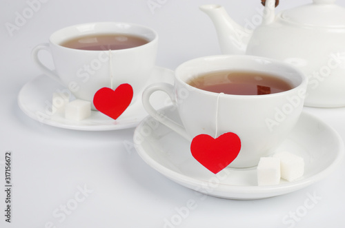 Two white cups of tea with red hearts labels on white.