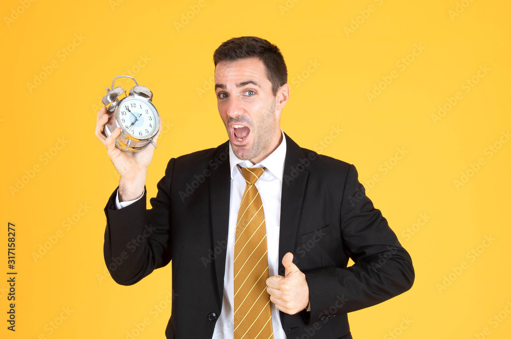 Portrait of a handsome businessman holding clock with thumbs up on yellow background. Portrait of a handsome businessman holding clock with thumbs up on yellow background.