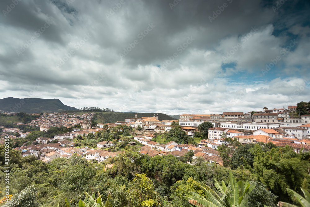Panorama of colonial mining city centre Ouro Preto in Minas Gerais, Brazil, with surrounding mountains in the background seen from a high vantage point against a blue sky with dramatic clouds above