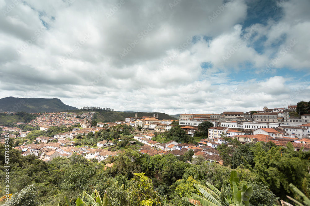 Panorama of colonial mining city centre Ouro Preto in Minas Gerais, Brazil, with surrounding mountains in the background seen from a high vantage point against a blue sky with dramatic clouds above