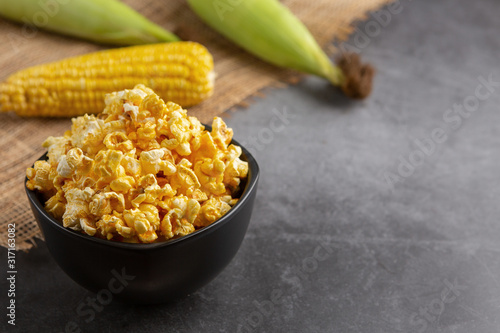 Popcorn in the black bowl and raw corn on the black table