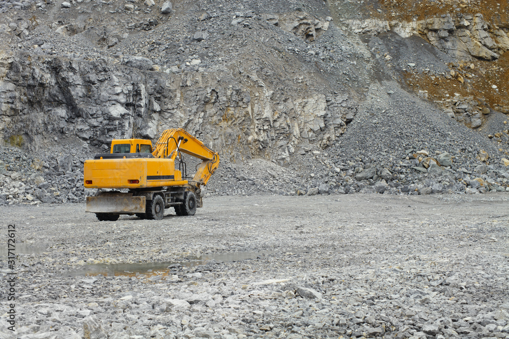 Wheel excavator with a hydraulic hammer rides inside a quarry for limestone mining, rear view. Quarry equipment. Mining industry. Wheel excavator with a hydraulic hammer rides inside a quarry for limestone mining, rear view. Quarry equipment. Mining industry.
