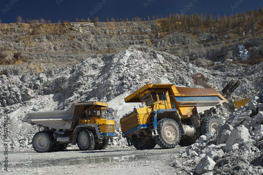 Two heavy quarry trucks inside a quarry for limestone mining, close-up. Heavy equipment. Mining industry. Two heavy quarry trucks inside a quarry for limestone mining, close-up. Heavy equipment. Mining industry.