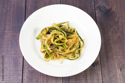 Zucchini spaghetti in a plate on a wooden background. Vegan food. Vegetable pasta