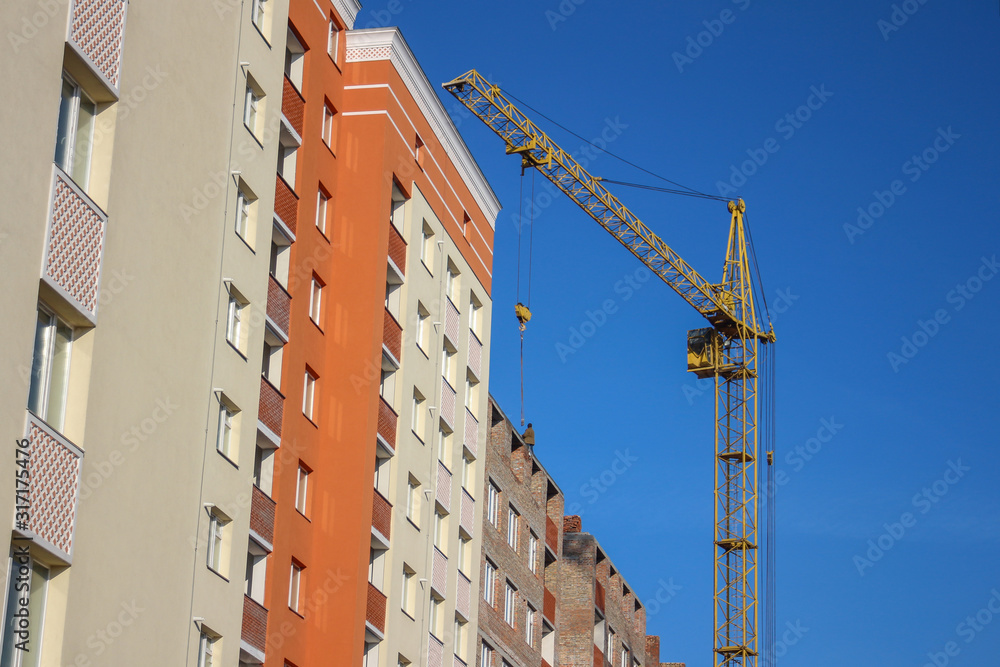 Crane and building construction site against blue sky. Unfinished building.  Extensive building, dormitory area, urban population growth, extinction of the village. Copy space