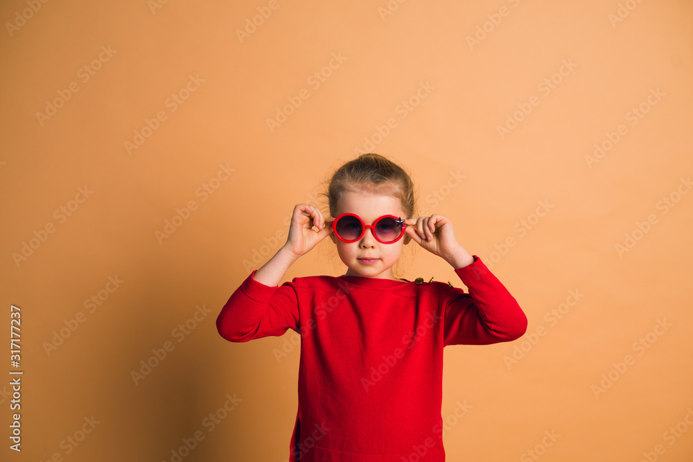 Studio shot of young fashion 6-7 year old blonde girl wearing sunglasses, on light brown background Studio shot of young fashion 6-7 year old blonde girl wearing sunglasses, on light brown background