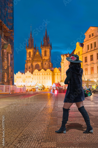 A woman in a black coat with a black hat and bag walks down the street -    Historical medieval astronomical clock in Old Town Square in Prague, Czech Republic