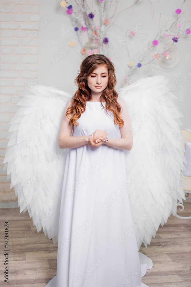 An angel in a white dress with wings behind his back is clasped hands in prayer. An angel in a white dress with wings behind his back is clasped hands in prayer.