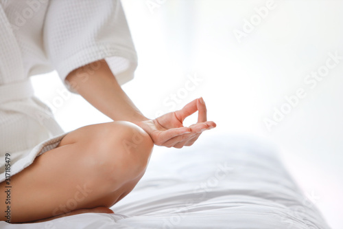 Young and calm woman in sleepwear hand enjoying in meditates with yoga pose on bed before go to bed or wake up. Cut girl sitting in white bedroom with relaxation. (lifestyle concept)