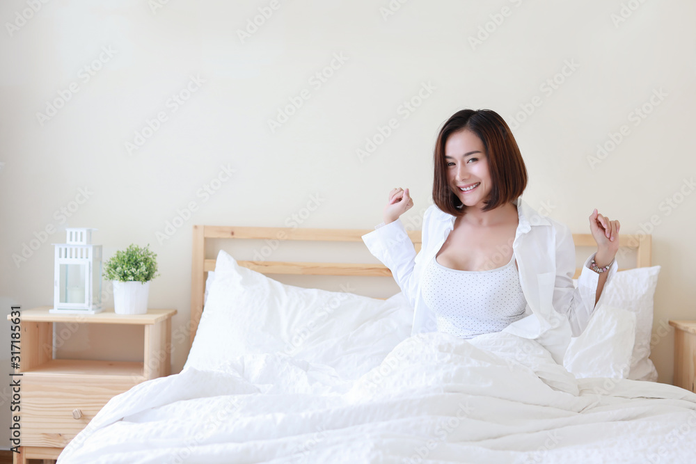 Front view beautiful and healthy young asian woman wake up in the morning, she stretching after wake up in the morning on white bed in bedroom. Lifestyle in bedroom concept Front view beautiful and healthy young asian woman wake up in the morning, she stretching after wake up in the morning on white bed in bedroom. Lifestyle in bedroom concept