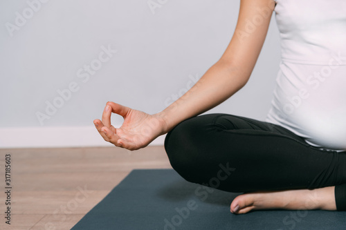 Close-up of pregnant woman meditating while sitting in lotus position. Meditating on maternity.