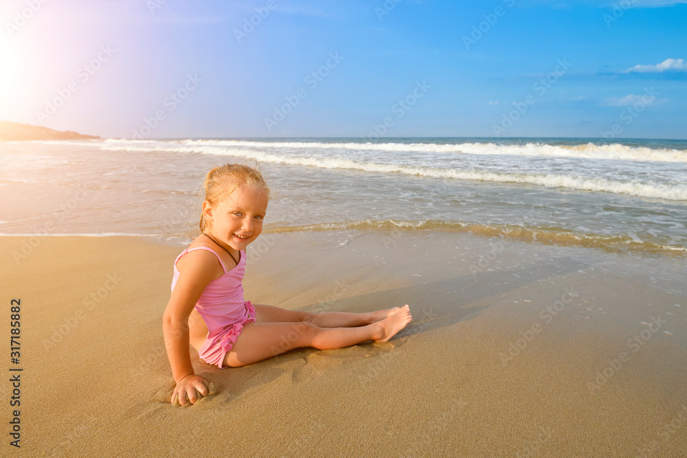 Little pretty Girl in pink swimsuit sitting on the beach in water waves and looking at the morning sea and sky Little pretty Girl in pink swimsuit sitting on the beach in water waves and looking at the morning sea and sky