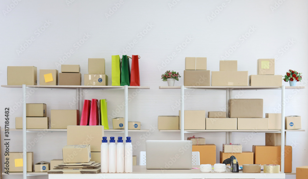Computer on wooden working table with package product box delivery background in room in apartment indoor. Startup small business SME concept Computer on wooden working table with package product box delivery background in room in apartment indoor. Startup small business SME concept