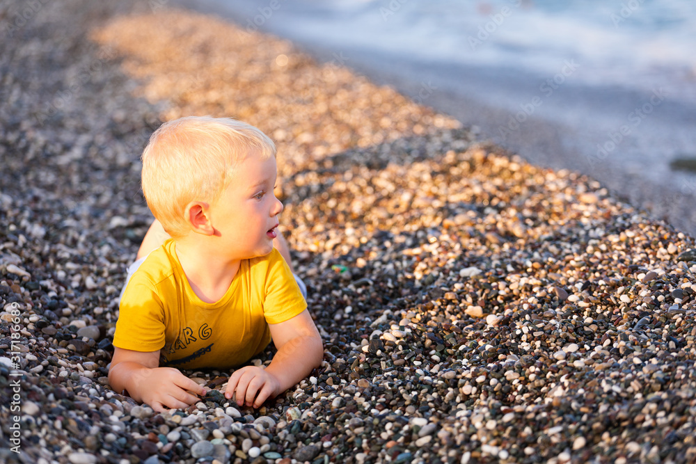 The boy lies on a pebble beach and looks at the sea The boy lies on a pebble beach and looks at the sea