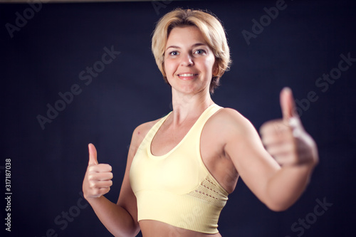 Woman in sport clothes smiling and showing thumb up gesture. Fitness and healthcare concept