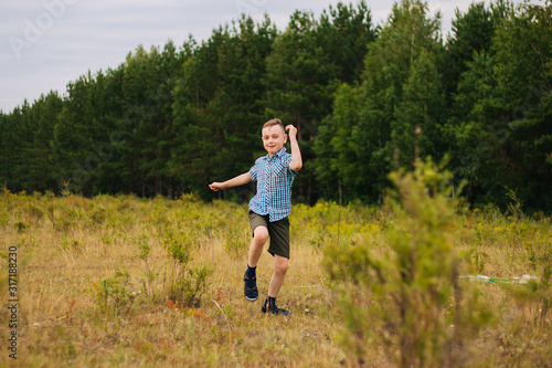 A boy in a blue plaid shirt runs across the field. The child plays in the fresh air.