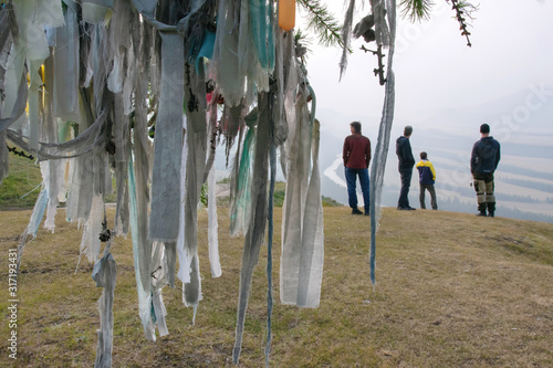 Prayers ribbons (Turkic: djalama or kyra) on the tree on a mountain pass and group of tourists. Argut river region, Altai Republic; Siberia, Russia. photo