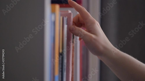 Hand reaches for and pulls classic book from library shelf