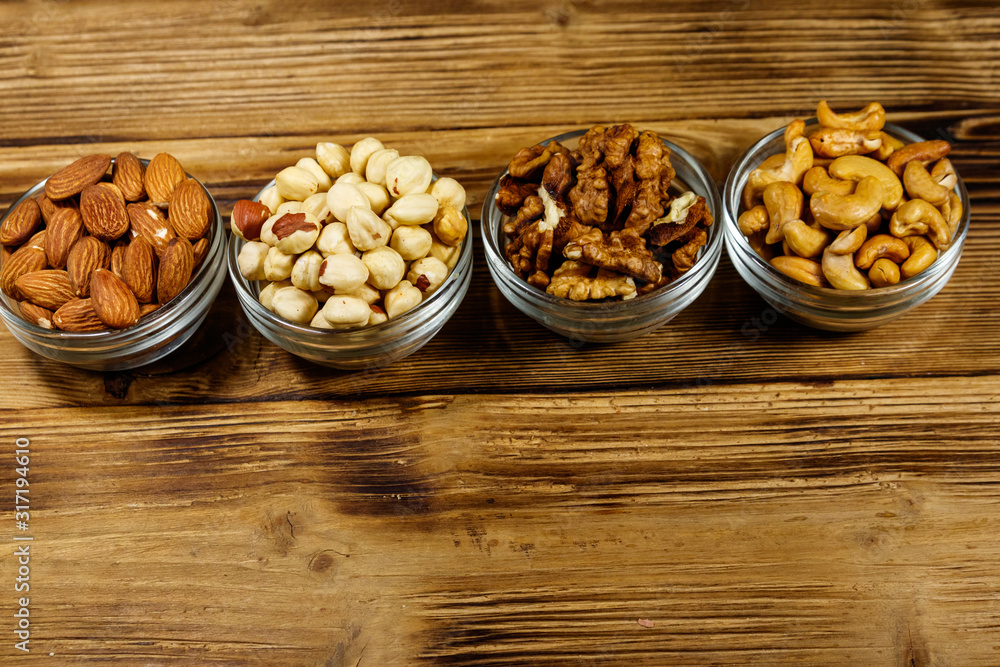 Assortment of nuts on wooden table. Almond, hazelnut, walnut and cashew in glass bowls. Healthy eating concept Assortment of nuts on wooden table. Almond, hazelnut, walnut and cashew in glass bowls. Healthy eating concept