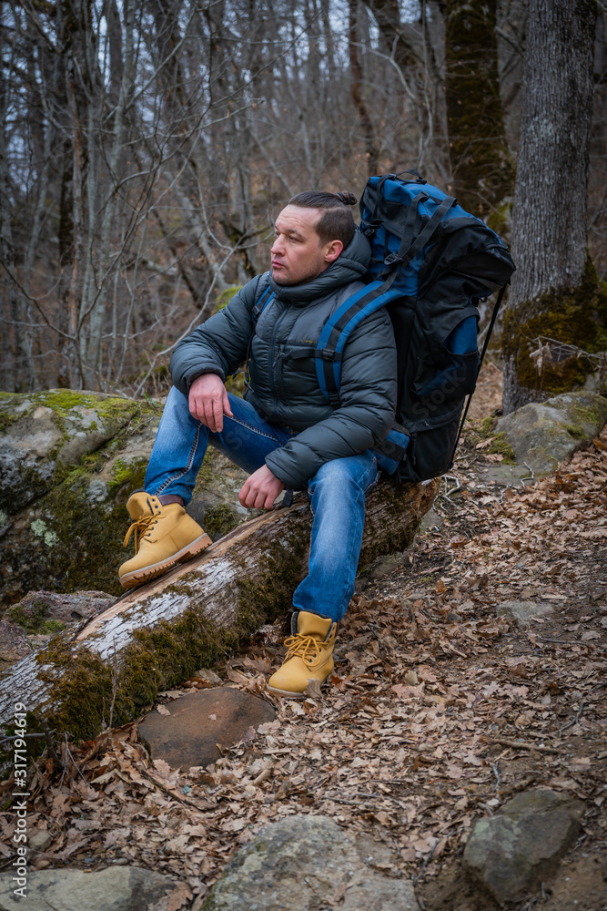 Hiker traveler sits on an old tree in a dense autumn forest Hiker traveler sits on an old tree in a dense autumn forest