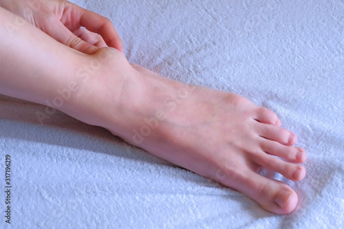 Fotografie Woman palpates hand leg ankle hygroma in joint, foot closeup view on white background