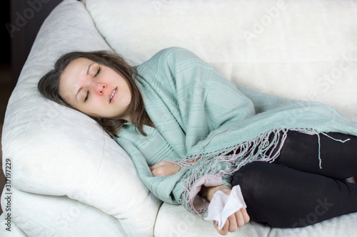 Sick, unhealthy woman with temperature lying on sofa at home under plaid