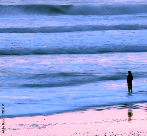 Silhouette of woman fishing in surf at beach