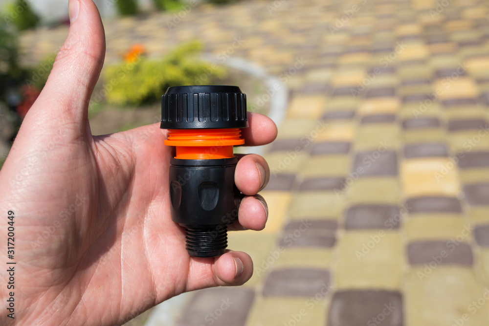 Fototapeta premium Connector in the male hand for a watering hose at the dacha. Close-up.