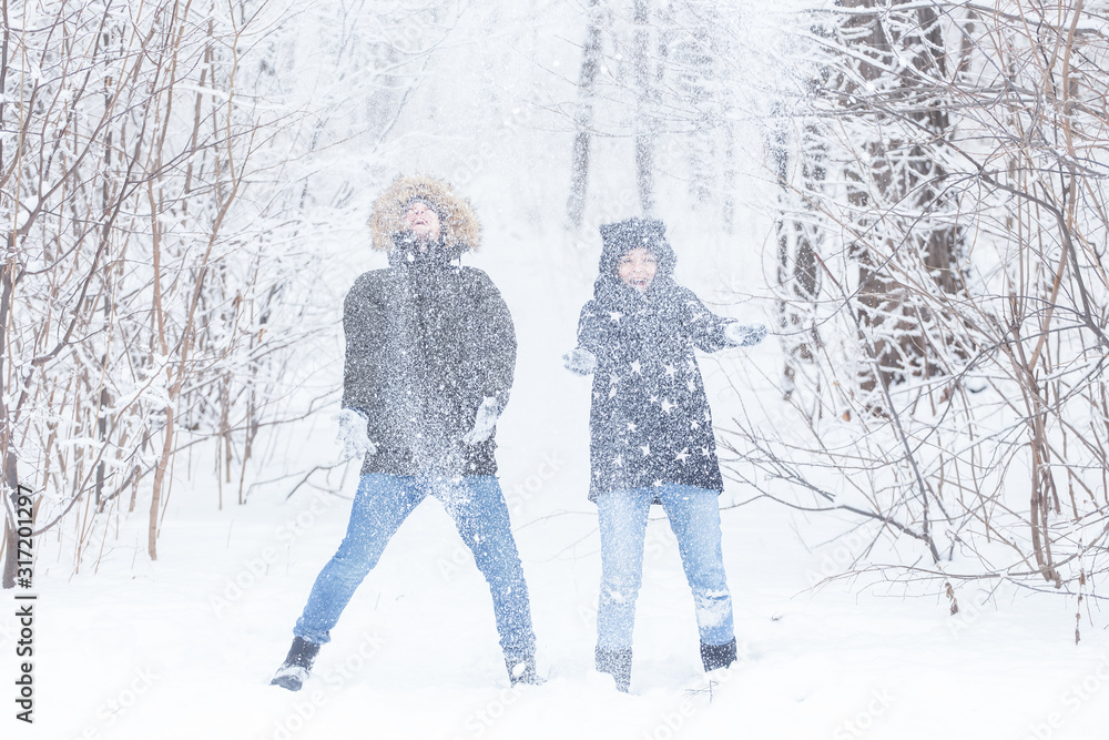 Love, relationship, season and friendship concept - man and woman having fun and playing with snow in winter forest