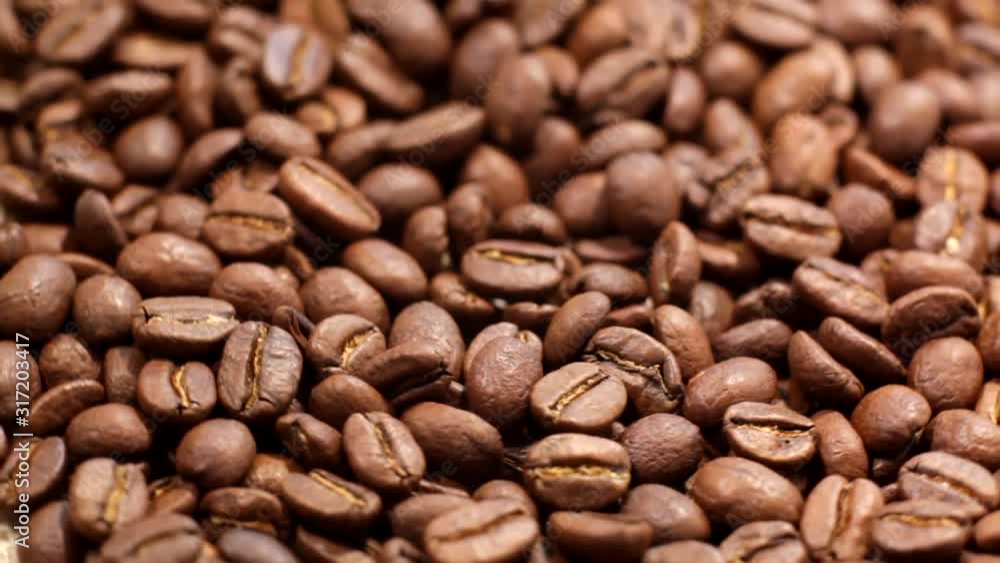 Close up of brown roasted coffee beans. Arabica coffee beans slowly spin. Premium quality light roasted coffee beans rotating. Close up of brown roasted coffee beans. Arabica coffee beans slowly spin. Premium quality light roasted coffee beans rotating.