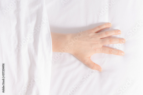 Woman's hand is visible from under the covers as a symbol of fight against insomnia. Tired and exhausted person falls asleep only in the morning. Snow-white bedding.