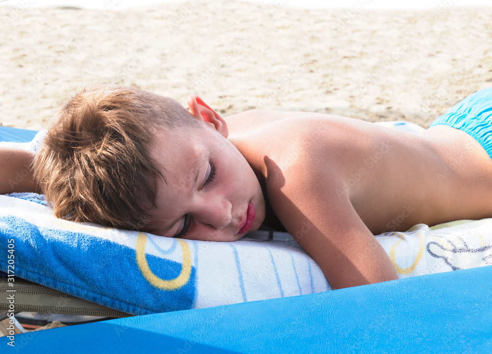 Fotka „A boy sleeps on the beach under strong sunlight. Danger of sunstroke  or burn. The risk of overheating and dehydration. Dangerous UV Sun Rays“ ze  služby Stock | Adobe Stock