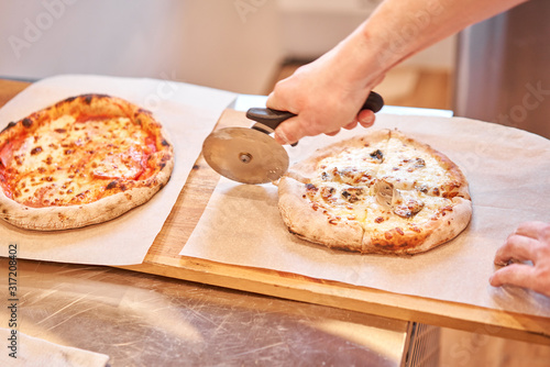 Italian kitchen and cooking concept. Chief with a pizza cutter cutting pizza to pieces at Neapolitan pizzeria. photo