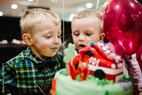 Portrait of happy boys celebrating birthday party blowing candles on cake. Fire truck, car and transportation theme boys party.
