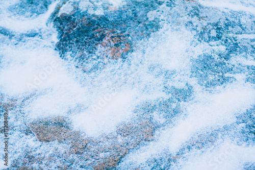 Snow on a stone, abstract defocused blured background in cold colors. Winter texture with snow and stone.