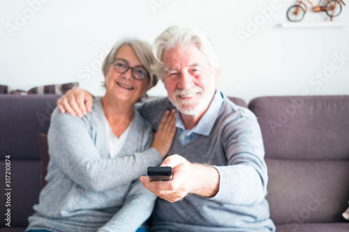 couple of two seniors or mature people together on the sofa at home watching the tv or some film or serie - man holding the remote control changing channel