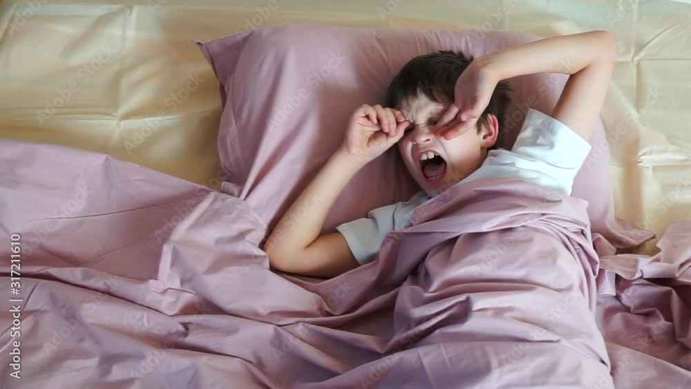 yawn child. boy wakes up. male child stretching in bed under blanket. good morning. cute male