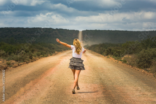 Happy woman walking and jumping on a long abandon country road enjoying and celebrating her freedome