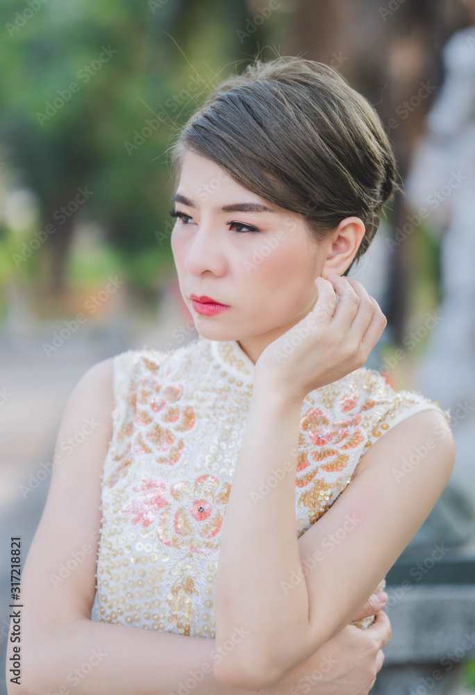 An Asian woman is wearing a cream-colored Chinese dress. Her eyes look at the side. Happy chinese new year. An Asian woman is wearing a cream-colored Chinese dress. Her eyes look at the side. Happy chinese new year.