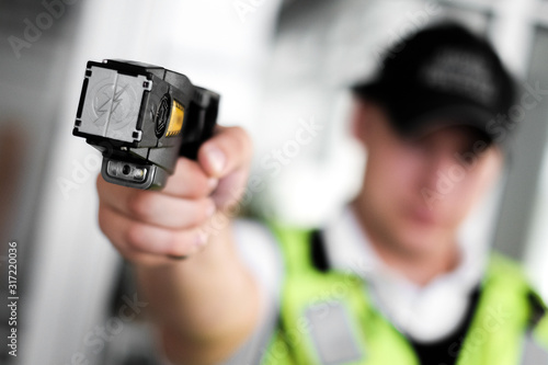 Closeup view of a loaded stun gun in a hand of a young man wearing high visibility vest photo