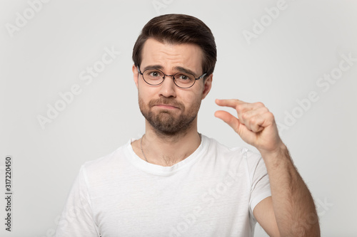 Disappointed millennial man in glasses showing small size length. photo